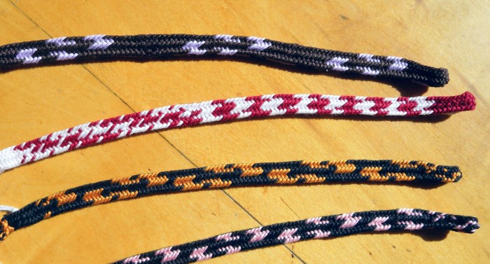 Side-slit shape variation of the 5-transfer braid. 3 turned loop transfers in the center area; 2 straight (open, unreversed) loop transfers - one at each edge of the braid.  Very asymmetrical bicolor loop color-patterns. Original braid structure, loopbraider.com. Fingerloop, loop-manipulation braiding.
